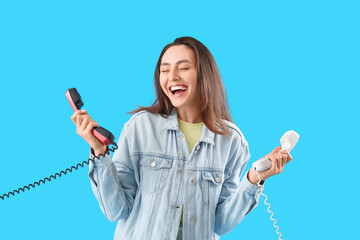 Happy young woman with telephone receivers on light blue background - obrazy, fototapety, plakaty