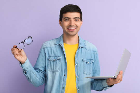 Male programmer with eyeglasses and laptop on lilac background