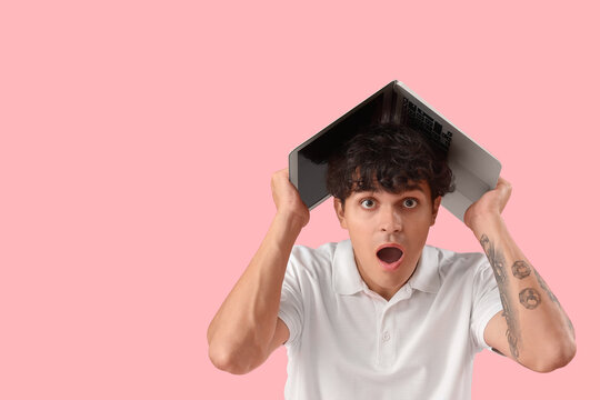 Shocked male programmer with laptop on pink background