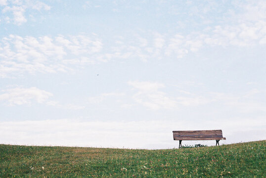 Wooden bench over grass lawn against blue sky in countryside