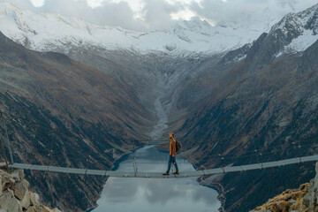 Man passing the bridge above the lake in Alps 