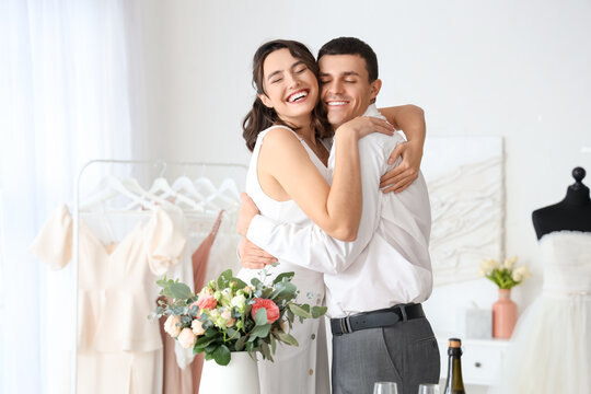 Young couple with wedding bouquet hugging in office