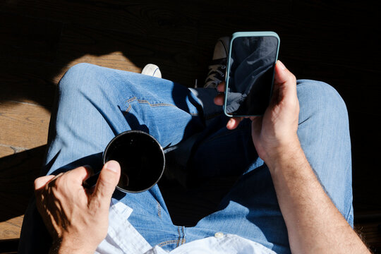 Anonymous man checking smartphone having coffee
