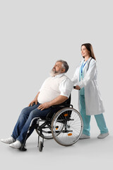 Mature man in wheelchair with nurse on light background