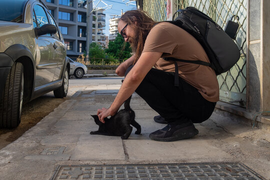 Male petting black cat on the street 