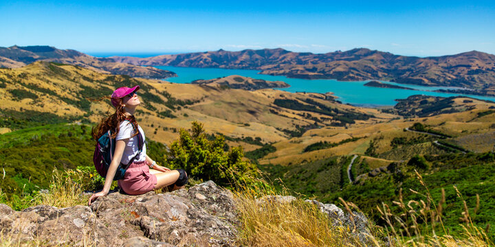 hiker girl admires the panorama of akaroa harbour and banks peninsula from the otepatotu scenic reserve, canterbury, new zealand south island near christchurch