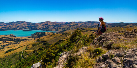 Fototapeta premium hiker girl admires the panorama of akaroa harbour and banks peninsula from the otepatotu scenic reserve, canterbury, new zealand south island near christchurch