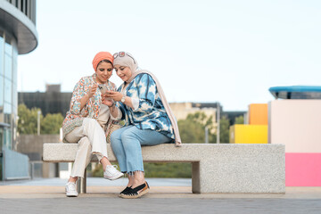 Portrait of happy muslim women friends using phone