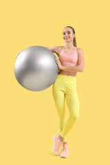 Portrait of female fitness trainer with fitball on yellow background