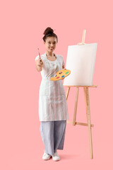 Female Asian artist with paint palette and easel on pink background