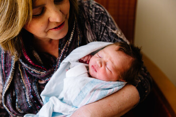 Grandmother holding newborn baby in hospital bed