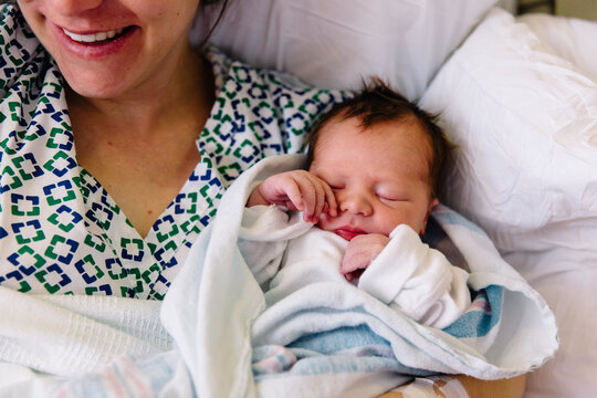 Mother smiles while holding newborn baby in hospital bed