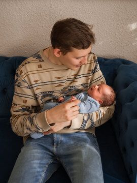 Happy father rocking newborn baby on couch