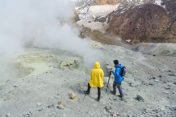 a man and a woman look at a bubbling mud cauldron on a volcano
