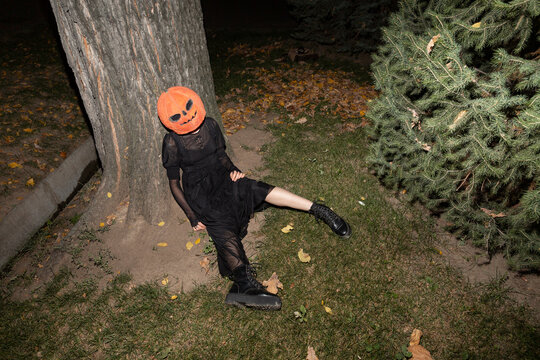 Woman in scary Halloween costume sitting against tree