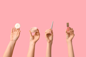 Female hands with lip gloss, powder and eyeliner on pink background