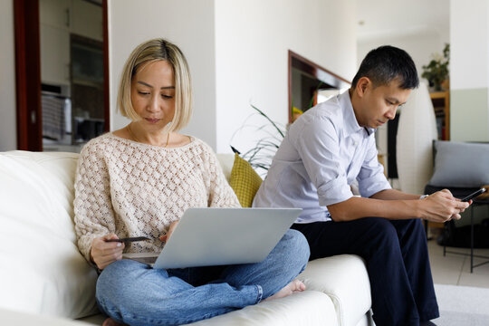 A couple sitting on the sofa with a laptop and a mobile phone