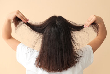Young woman with dandruff problem examining her hair on beige background, back view