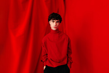 Serious young man standing near red background in studio