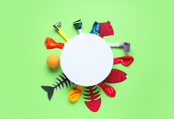 Blank card with paper fishes, balloons and party whistles on green background. April Fools Day...