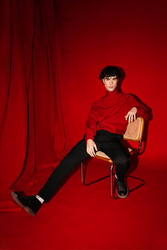 Stylish young male model sitting on chair against red