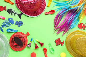 Frame made of wig, hats and party decor on green background. April Fools Day celebration
