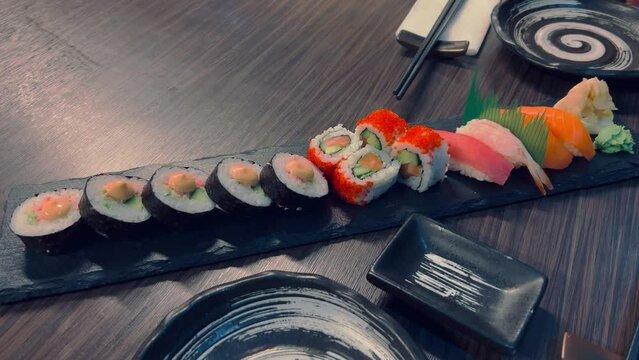 Sushi and rolls in plate. Close-up of sushi rolls on rectangle sushi plate. A set of fresh sushi rolls with salmon, avocado and black sesame seeds served on a plate with chopsticks. Japanese seafood 