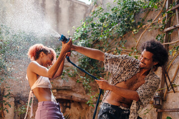 Black couple teasing each other playing with a water hose in summer