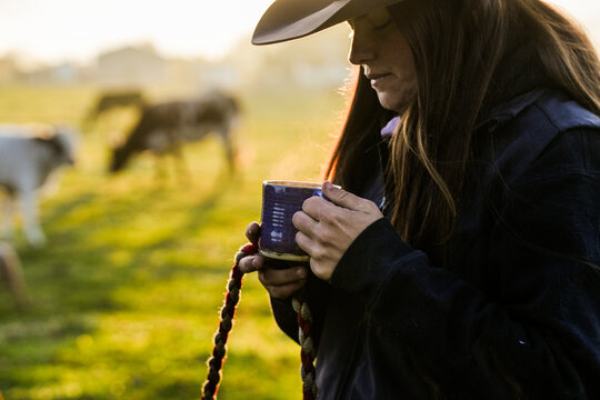 female rancher holds hot coffee cup at dawn 