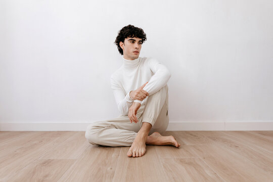 Stylish man sitting on parquet floor in light room