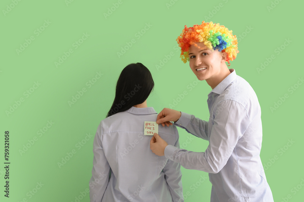 Poster Business man sticking paper on his colleague's back against green background. April Fools' Day celebration