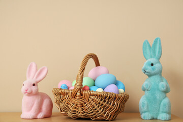 Painted eggs in basket and Easter bunnies on table near beige wall