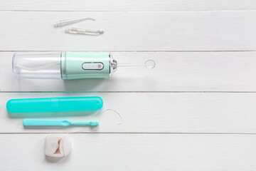 Oral irrigator, toothbrush, toothbrush case and dental floss on white wooden background