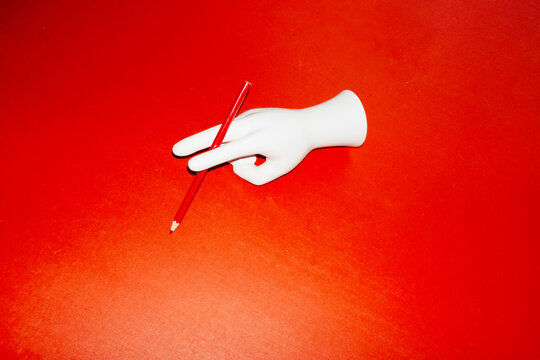 Porcelain hand holding a red pencil with hard direct flashlight