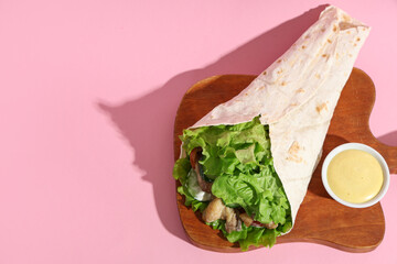 Tasty doner kebab and sauce on pink background