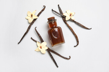Vanilla extract in bottle with vanilla pods and flowers on pink background. Top view