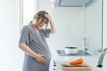 キッチンで頭痛・片頭痛に悩む妊娠後期の妊婦の女性
