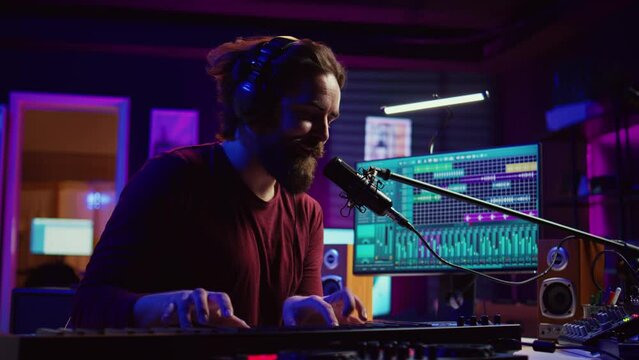 Musician playing piano midi controller and recording a new song, singing on microphone in his home studio. Sound engineer working on digital audio workstation, using electronic keyboard. Camera B.