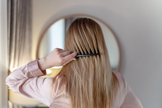 woman combing blond hair in bedroom
