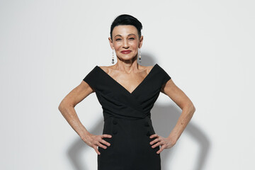Elegant senior woman in black dress striking a confident pose with hands on hips for camera portrait