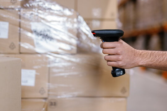 Unrecognizable person grasping handheld scanner cardboard boxes