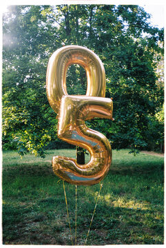 Golden number-shaped balloons floating in a park on a sunny day