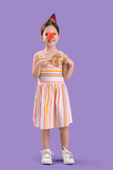 Cute little girl with clown nose, party hat and paper fish on lilac background. April Fool's Day celebration