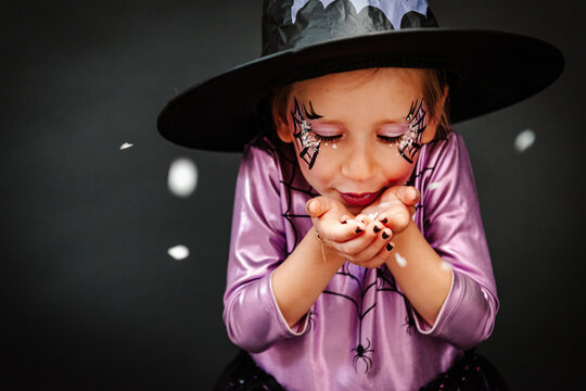 Girl with witch outfit, hat and face-paint blowing confetti around