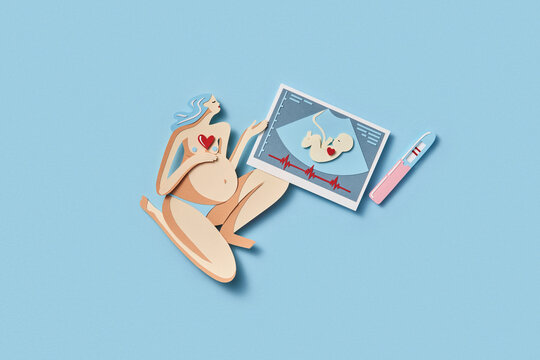 Papercraft figure of pregnant woman holding sonogram of her baby