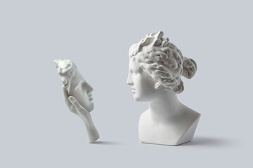 Plaster hand holding mask of human face in front of antique bust