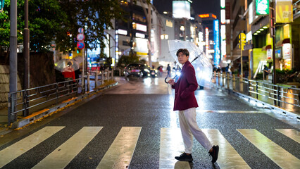 Portrait of Young Asian man holding umbrella walking city street crosswalk with night lights in...