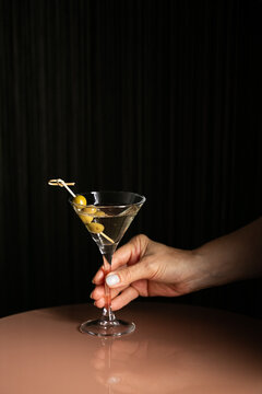 Woman holding martini cocktail drink with olives with hand