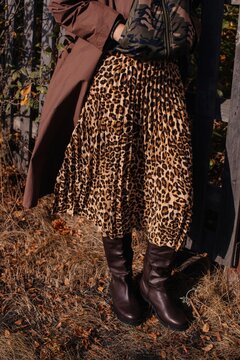 Crop woman in coat and leather boots standing on dry grass land
