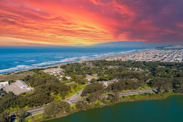 Foto auf Acrylglas aerial shot of a beautiful spring landscape at Lake Merced with vast blue ocean water a sandy beach, green trees and grass and cars on the street in San Francisco California USA © Marcus Jones